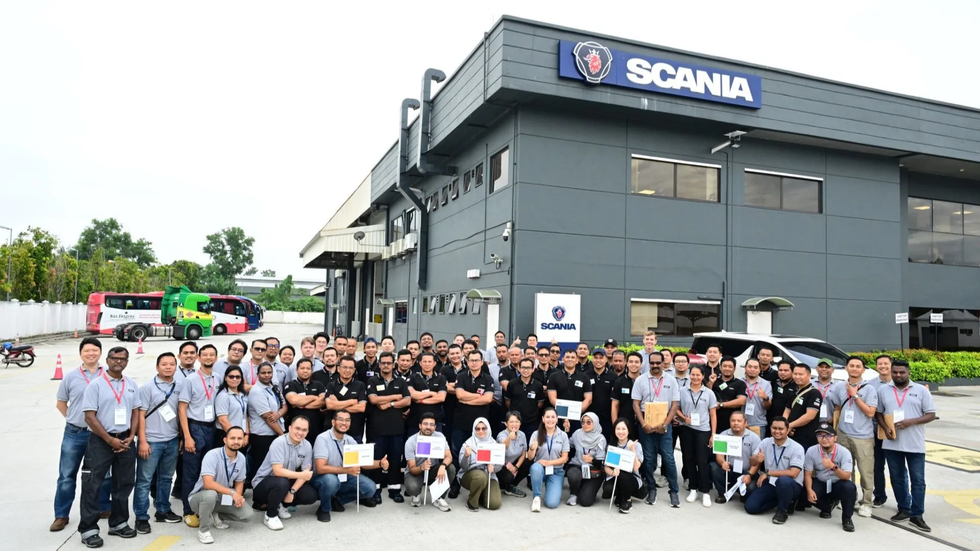 Group photo of Scania Malaysia staff and participants standing in front of a Scania service center, including Team Land Below the Wind from Kota Kinabalu, winners of the Scania Top Team Malaysia national finals.