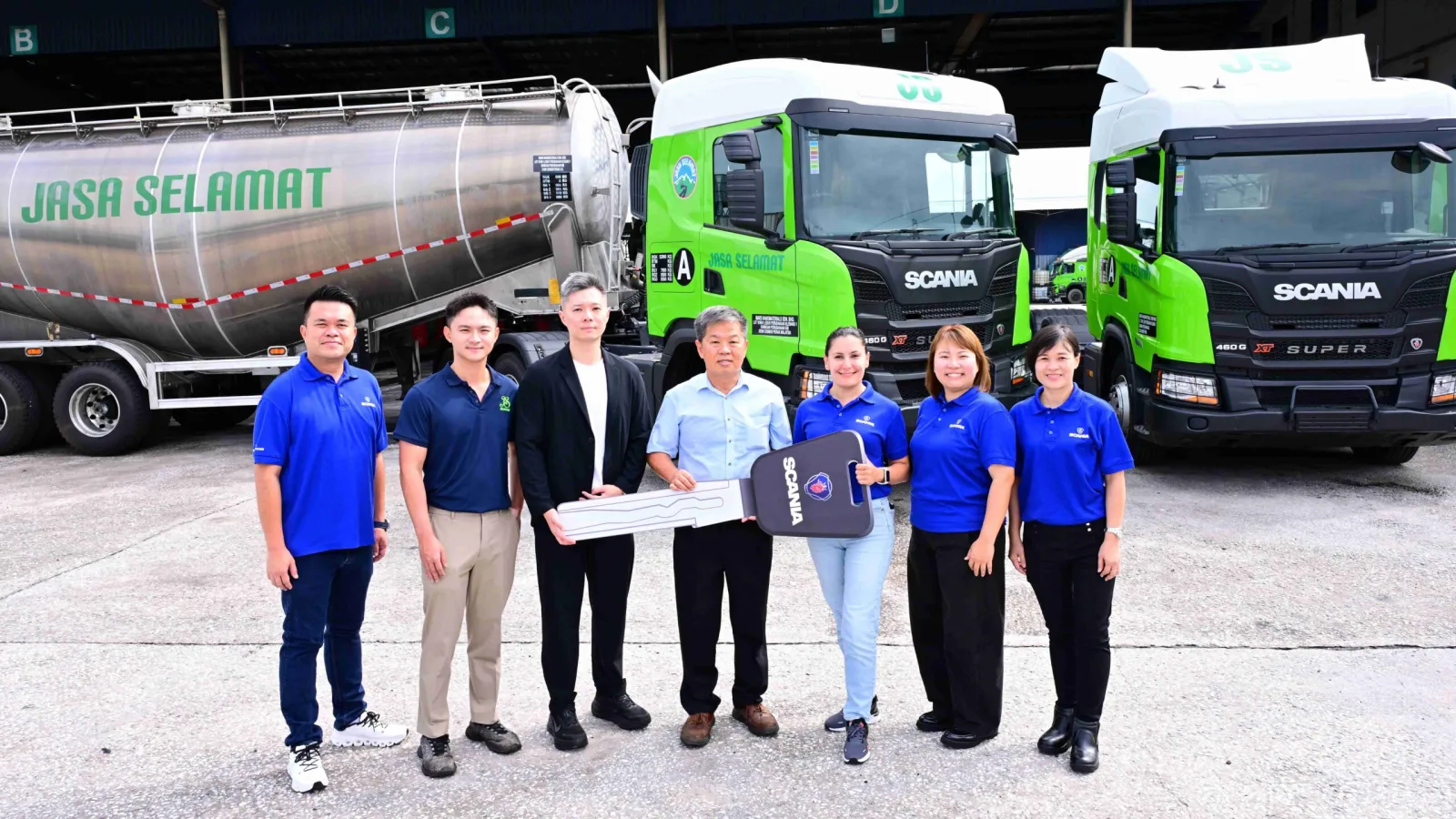 Executives from Syarikat Jaya Selamat and Scania Southeast Asia holding a ceremonial key mockup in front of green Scania Super G460 cement tanker trucks. (Photo: Scania Southeast Asia)