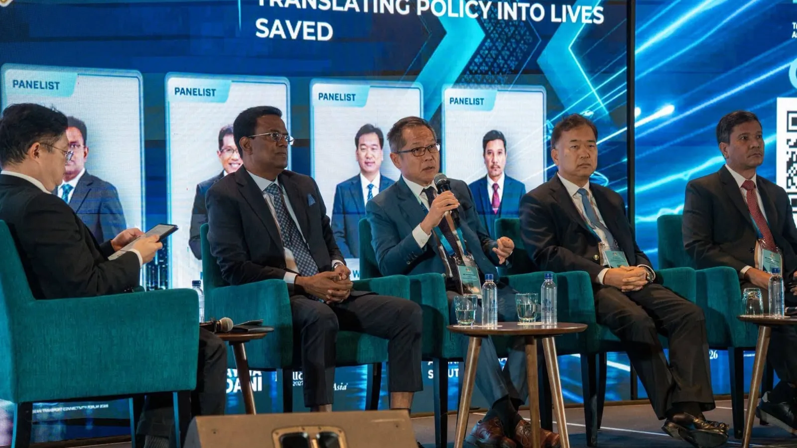 Panellists in suits seated in teal armchairs on stage during a technical forum at Road Safety Congress 2026 with digital backdrop text reading "Translating Policy into Lives Saved".