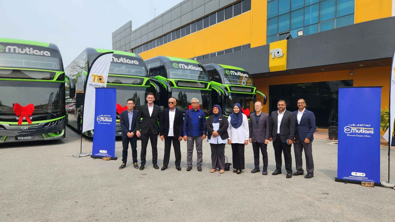Official handover group photo featuring executives standing in front of four green and black E-Mutiara MAN double-deck coaches decorated with red ribbons.